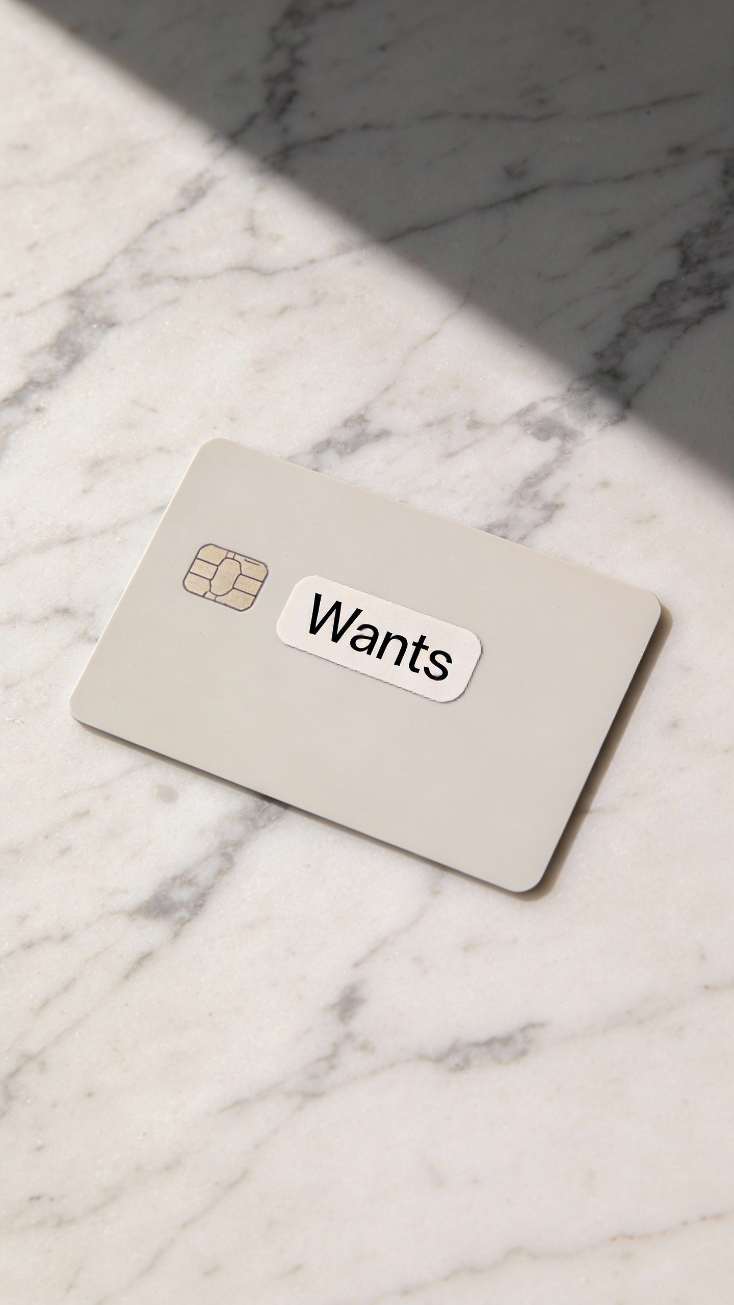 minimalist debit card with “Wants” sticker on marble surface