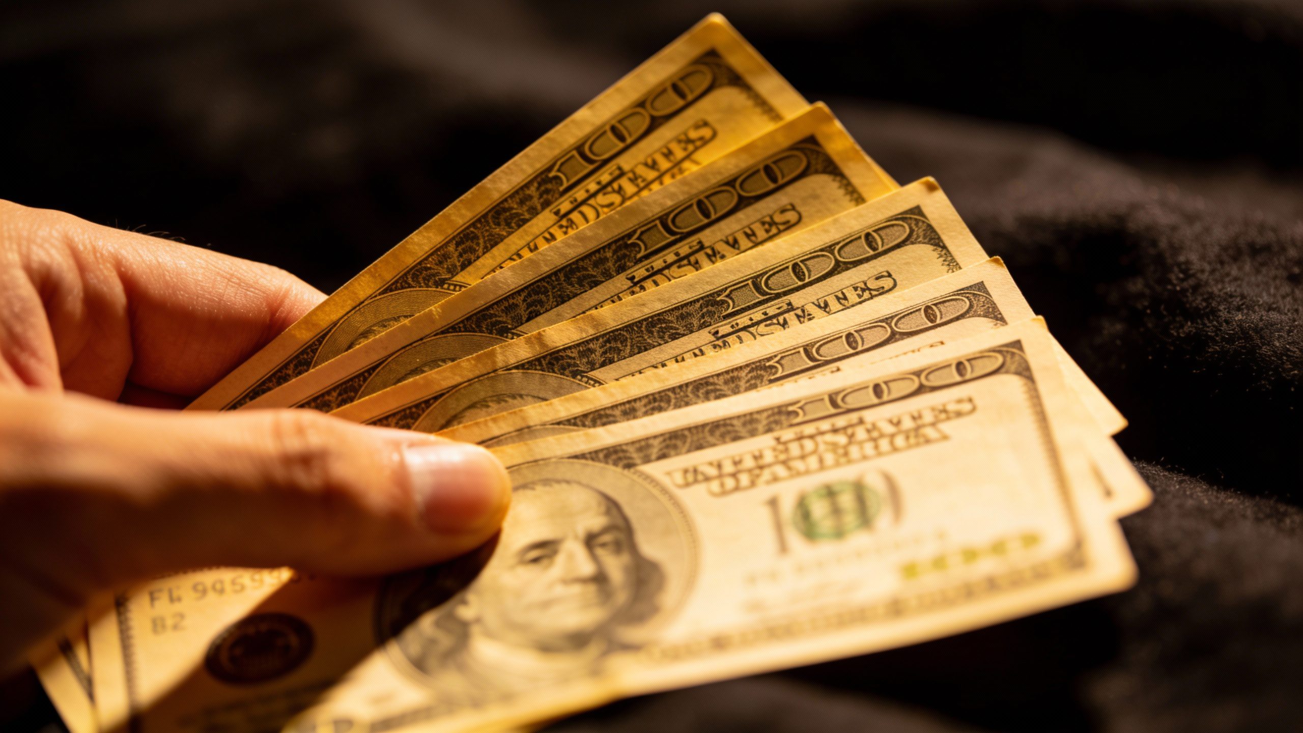 **Hand holding crisp dollar bills against dark fabric**