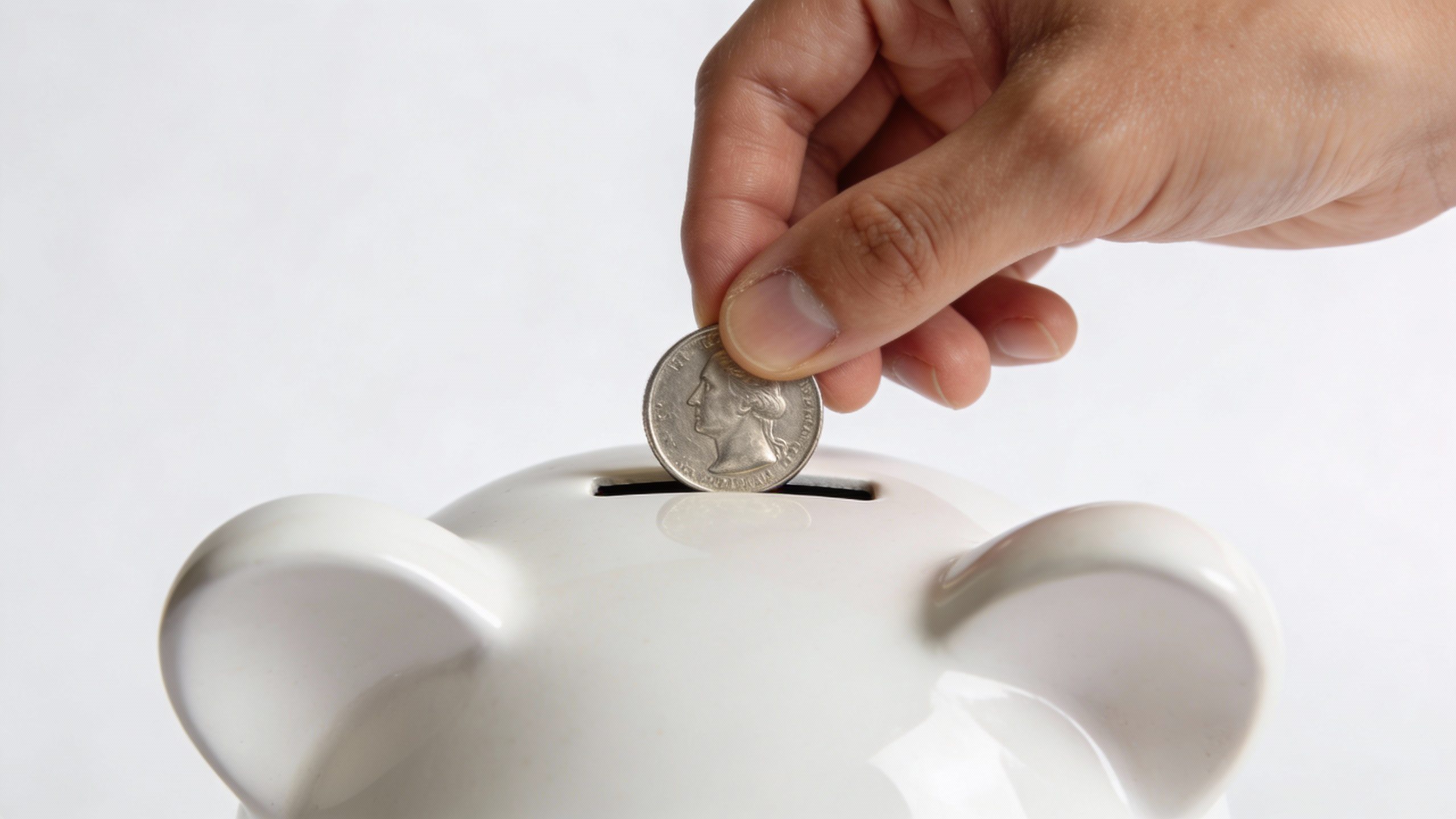 steady hand placing one coin into simple white piggy bank