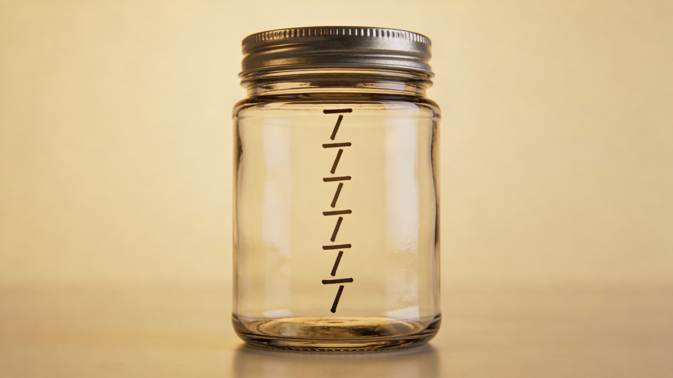 single glass jar labeled “Vacation Fund” with rising tally marks