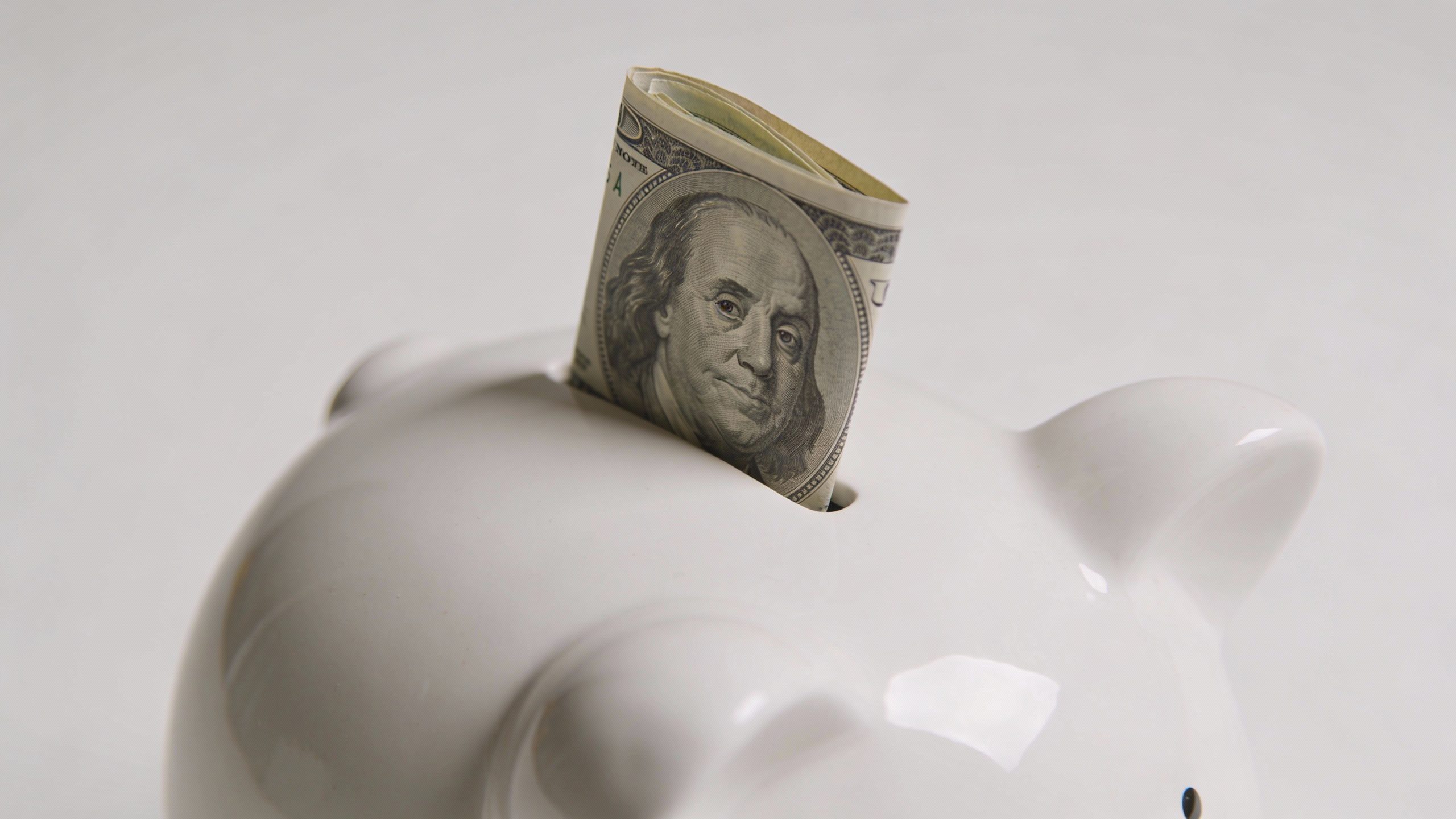 single white ceramic piggy bank with one folded $100 bill