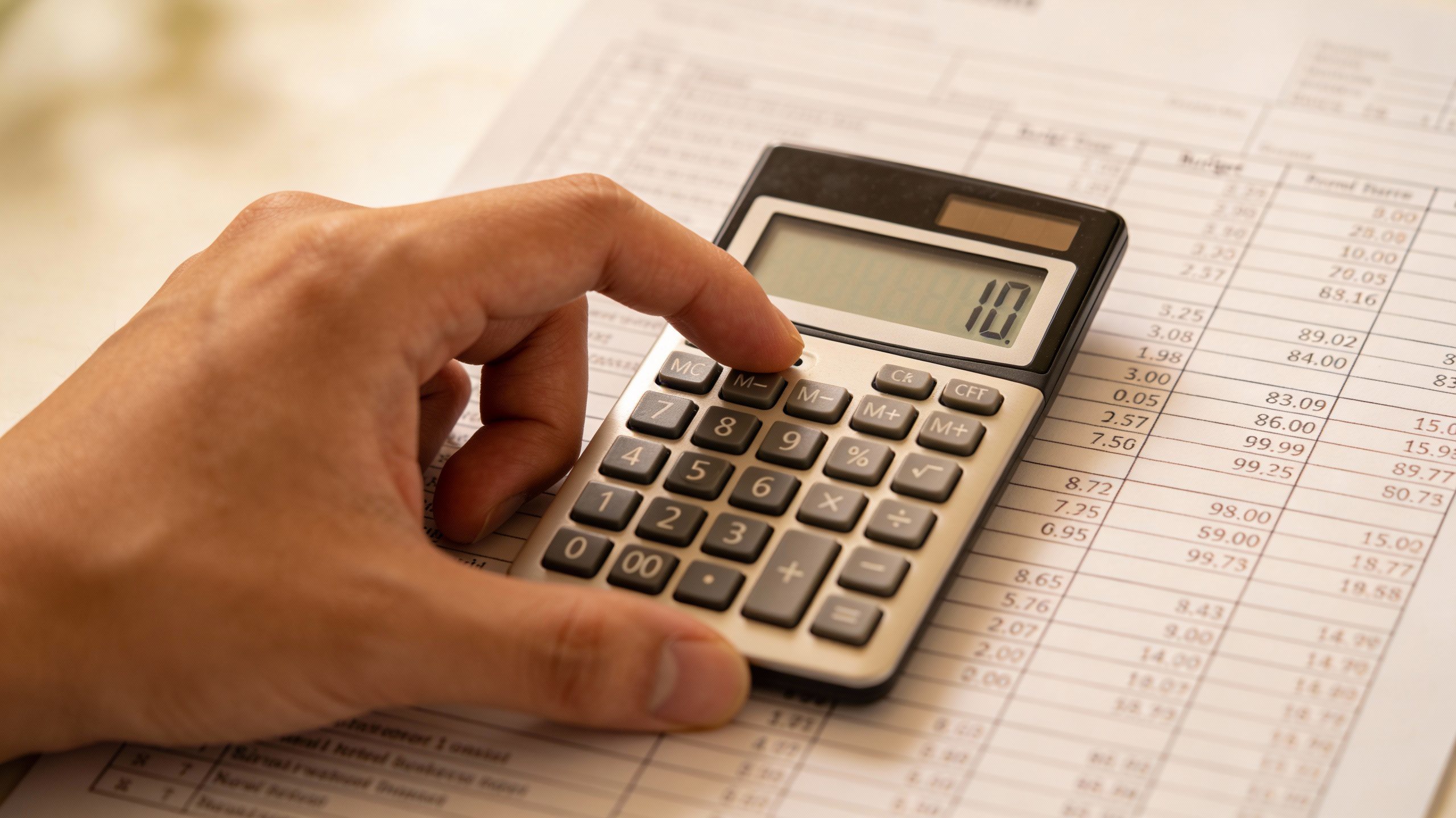 **Hand holding a calculator with budget spreadsheet**