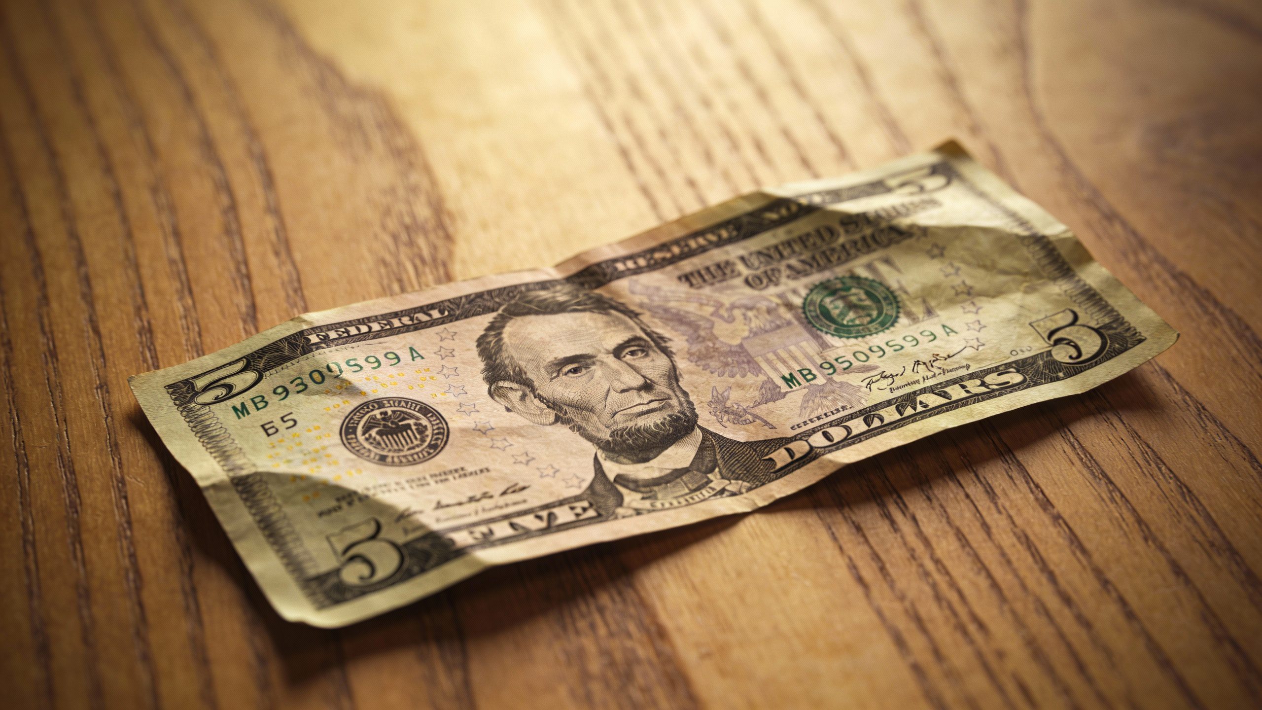 **Single crumpled $5 bill on wooden table**