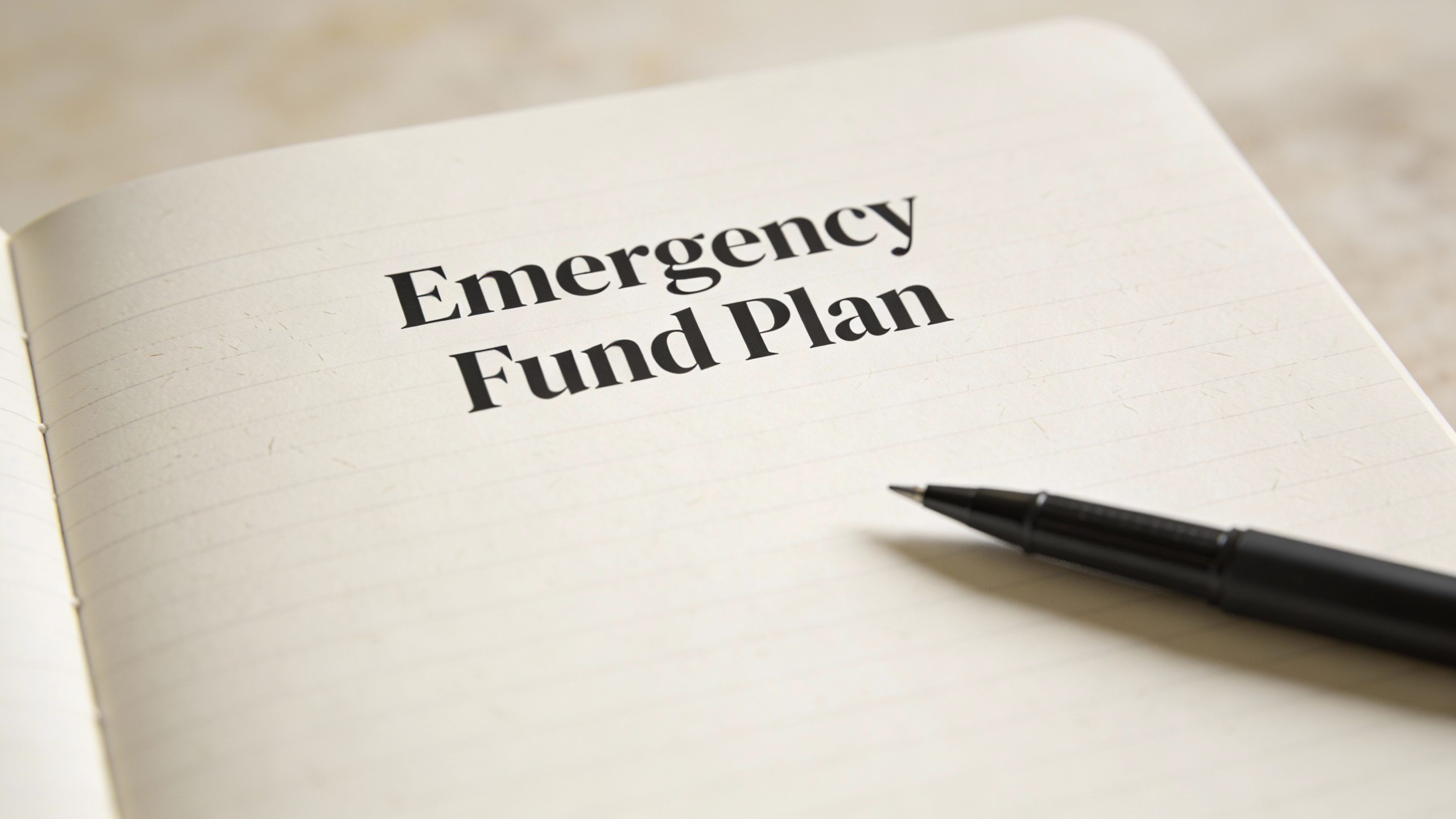 Closeup of a solitary notebook page titled “Emergency Fund Plan” with a pen beside