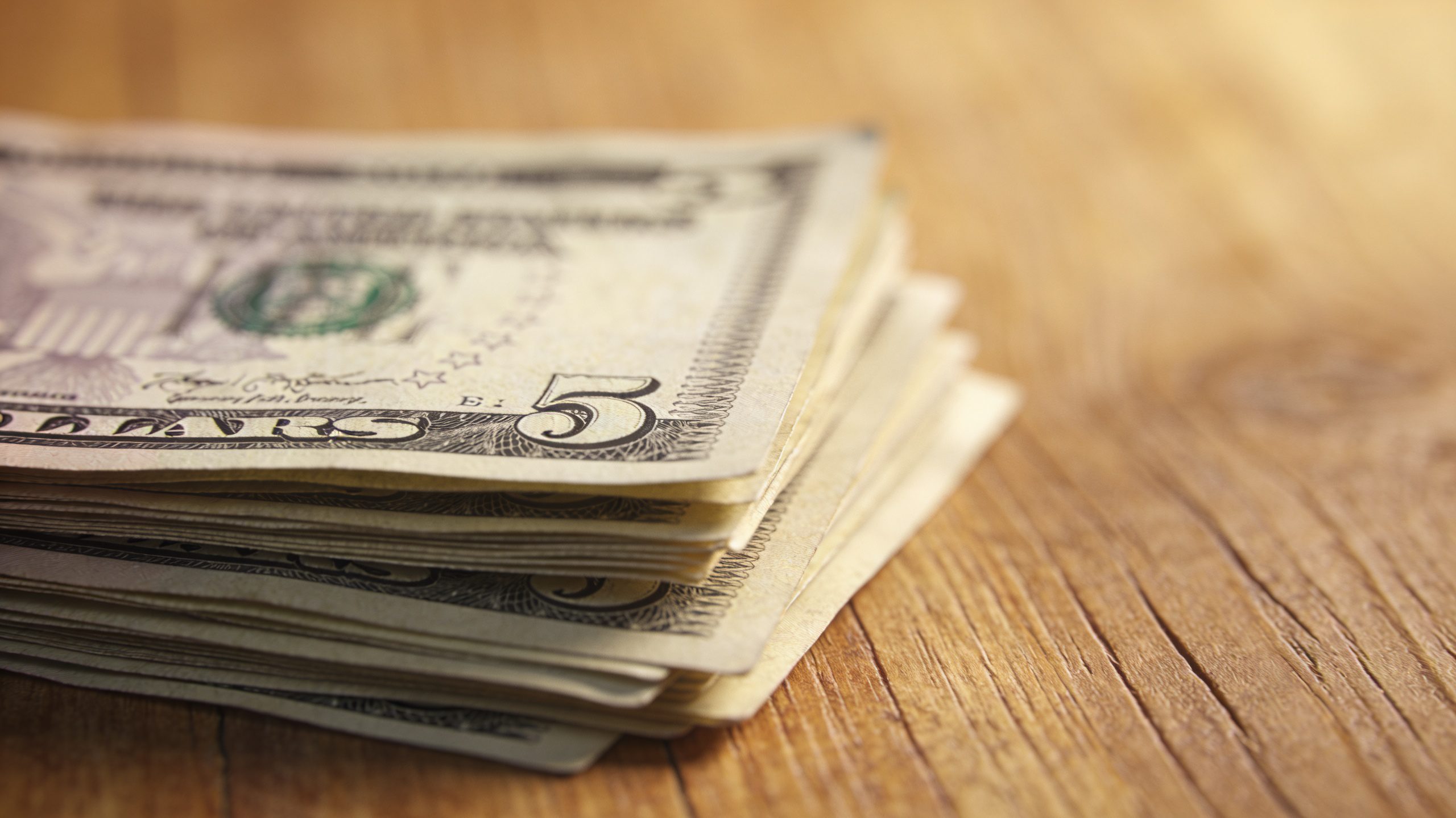 **Closeup of stacked $5 bills on wooden table**