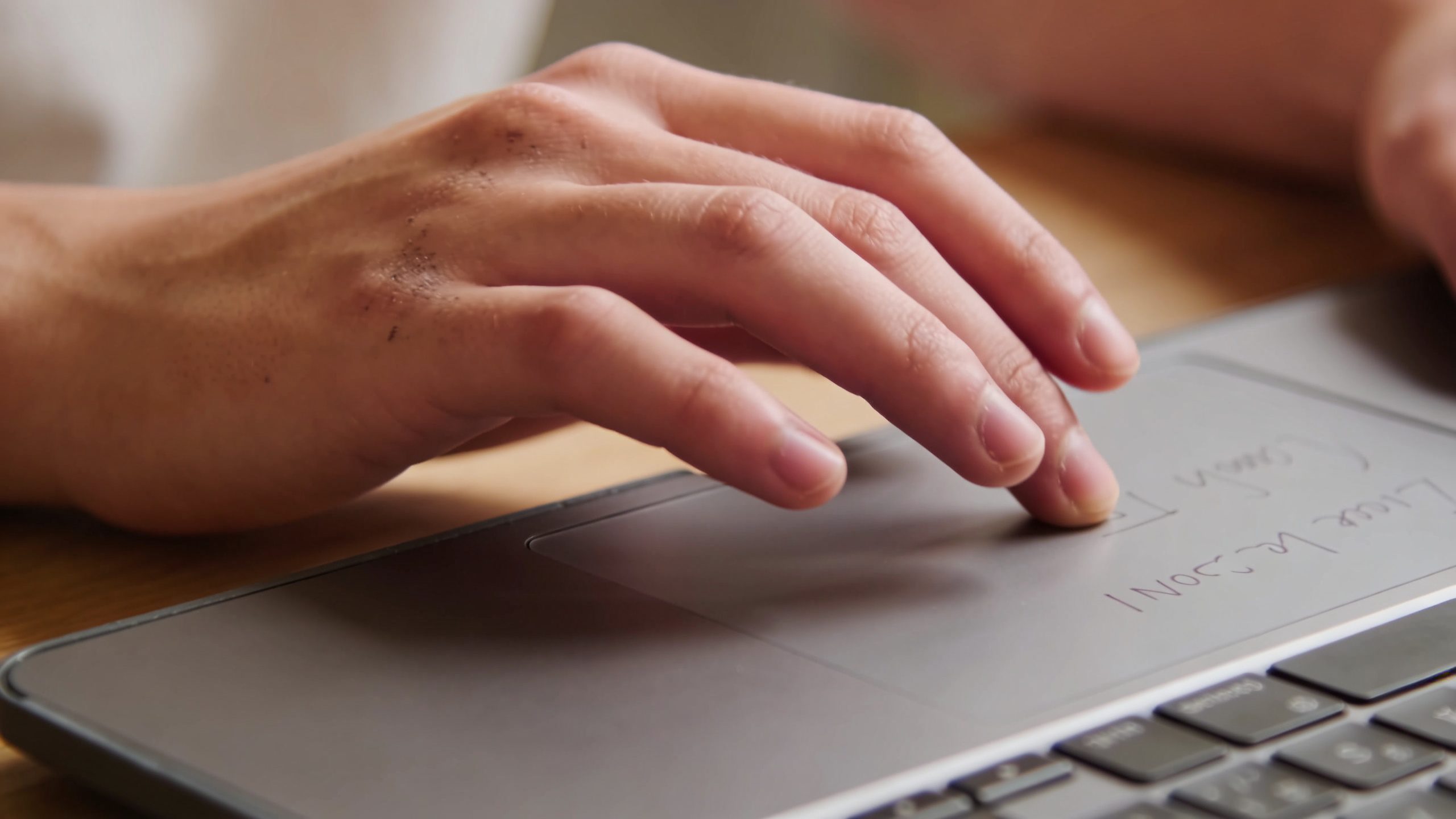 closeup of a student’s hand writing invoices on laptop trackpad