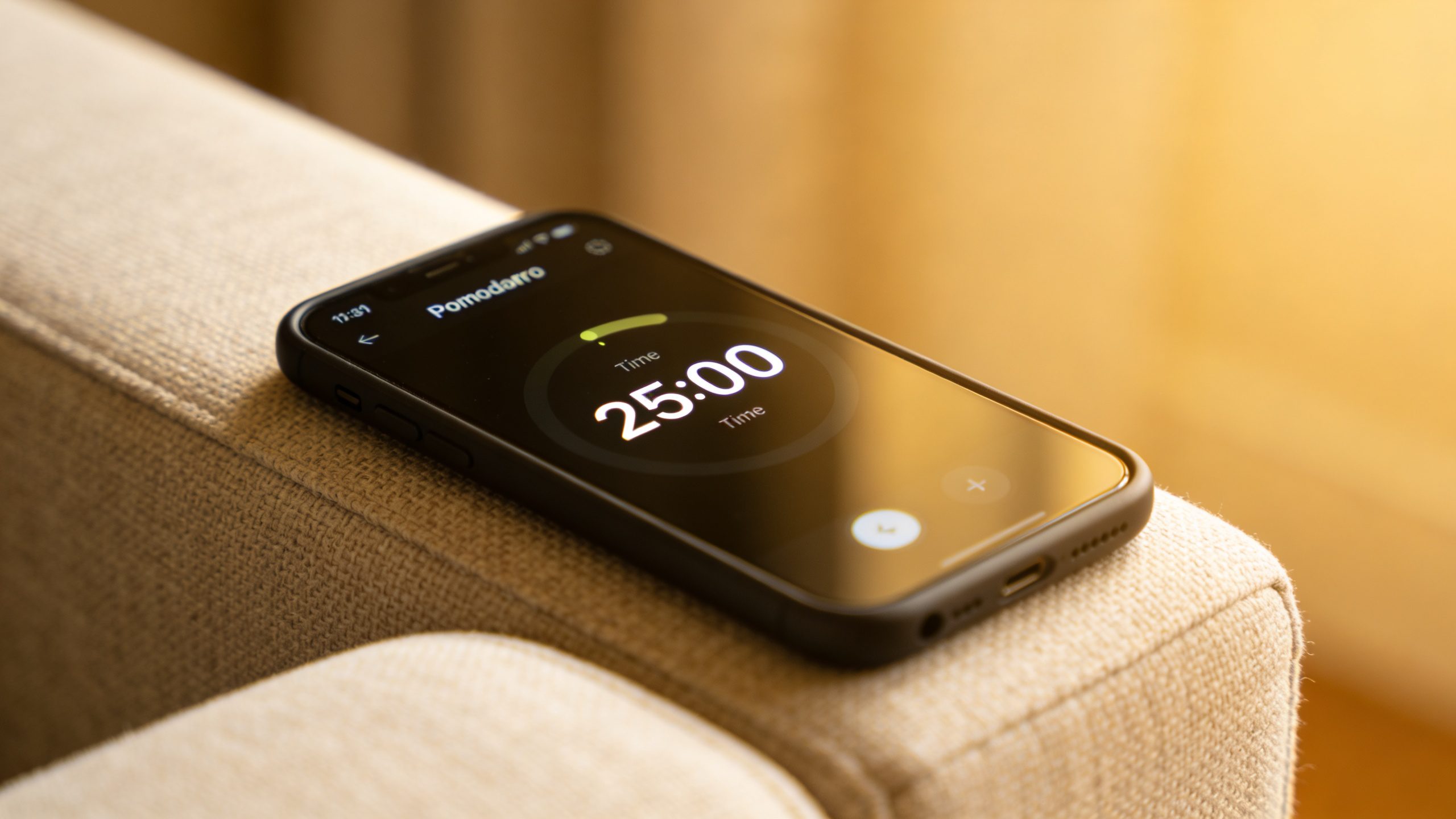 smartphone timer app showing 25:00 Pomodoro, on couch armrest