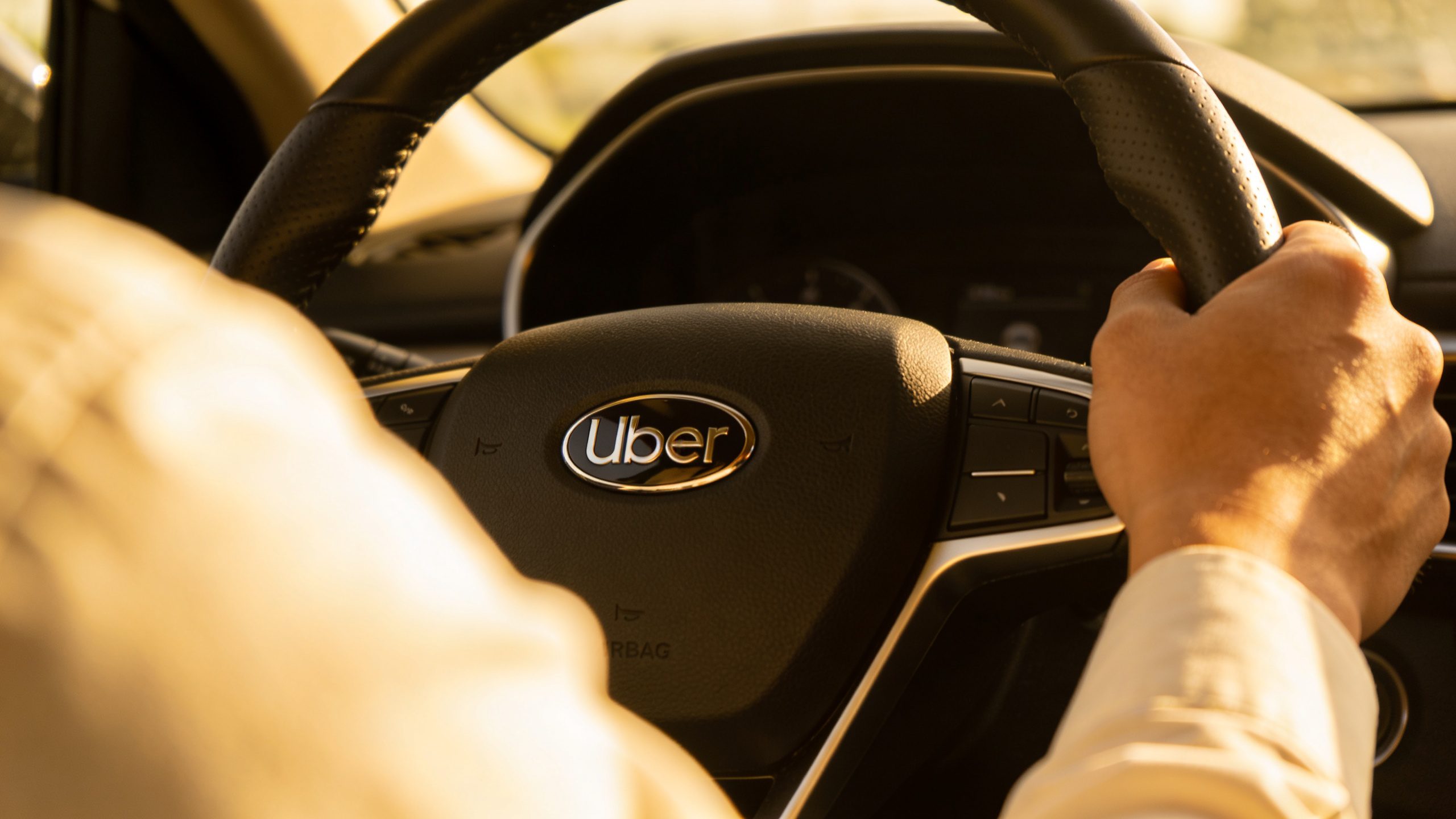 driver’s hand gripping Uber steering wheel emblem, shallow depth of field