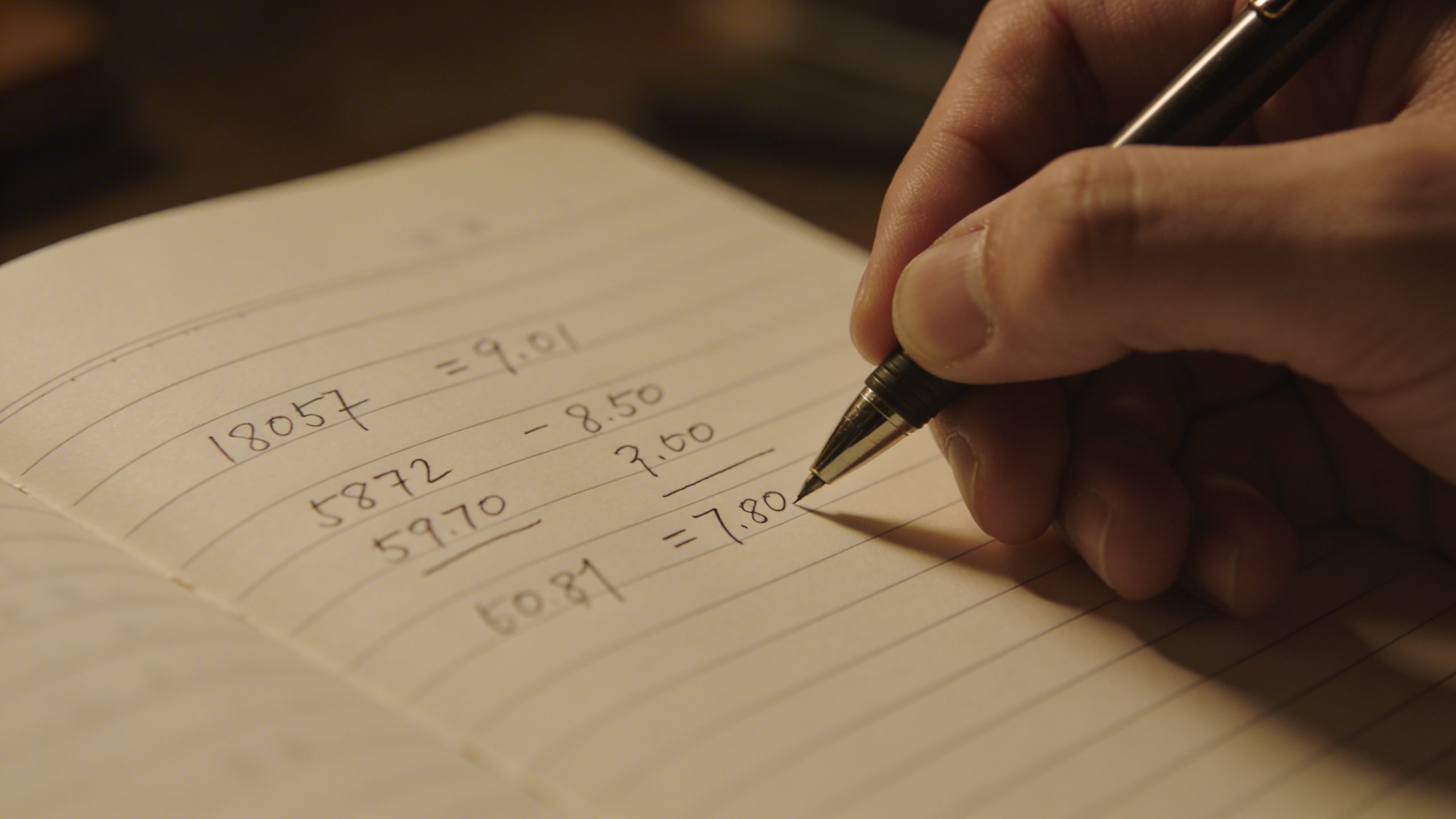 Closeup of a hand writing a personal budget in a notebook