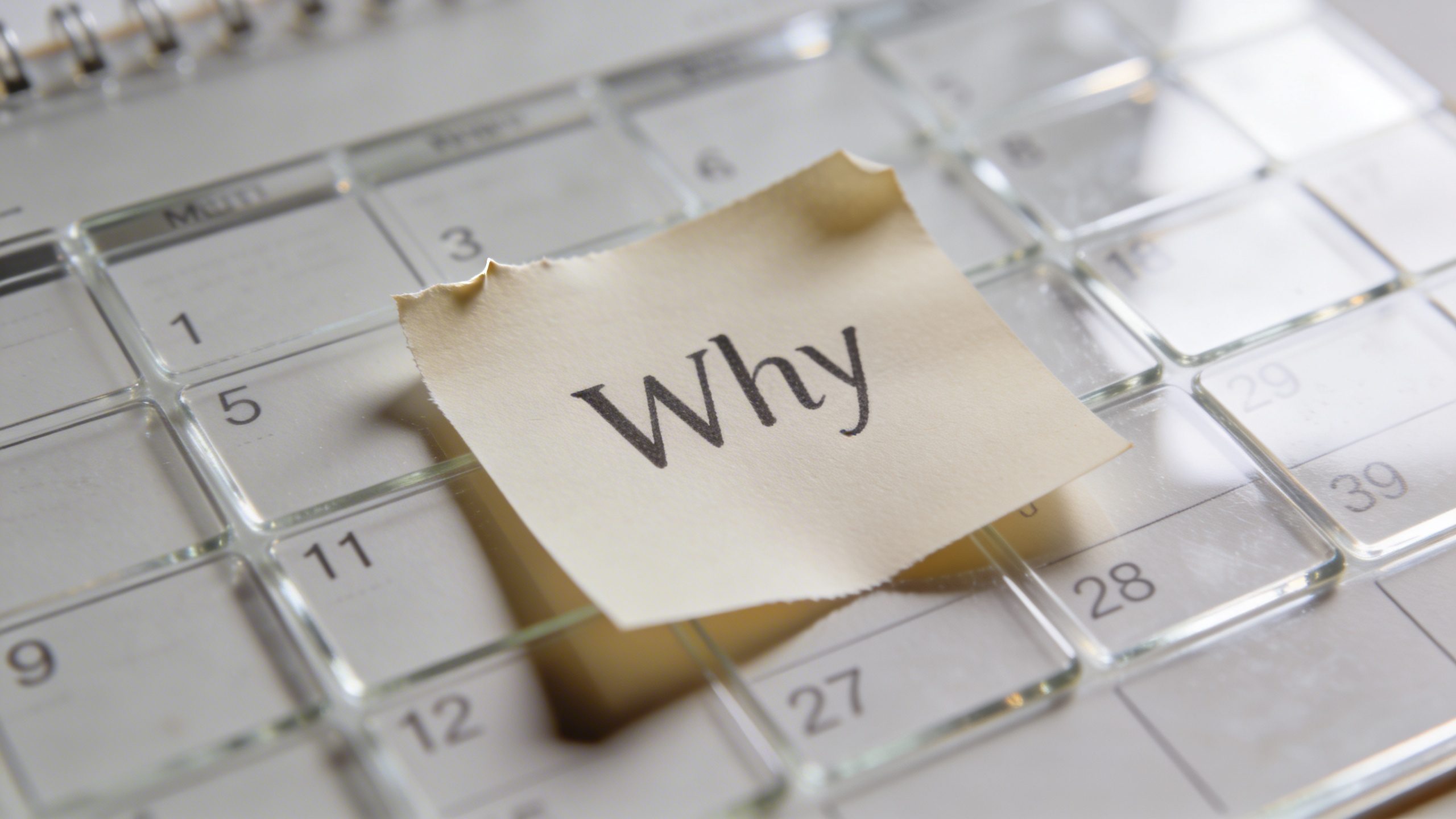 Closeup of a single sticky note labeled “Why” on a glass calendar