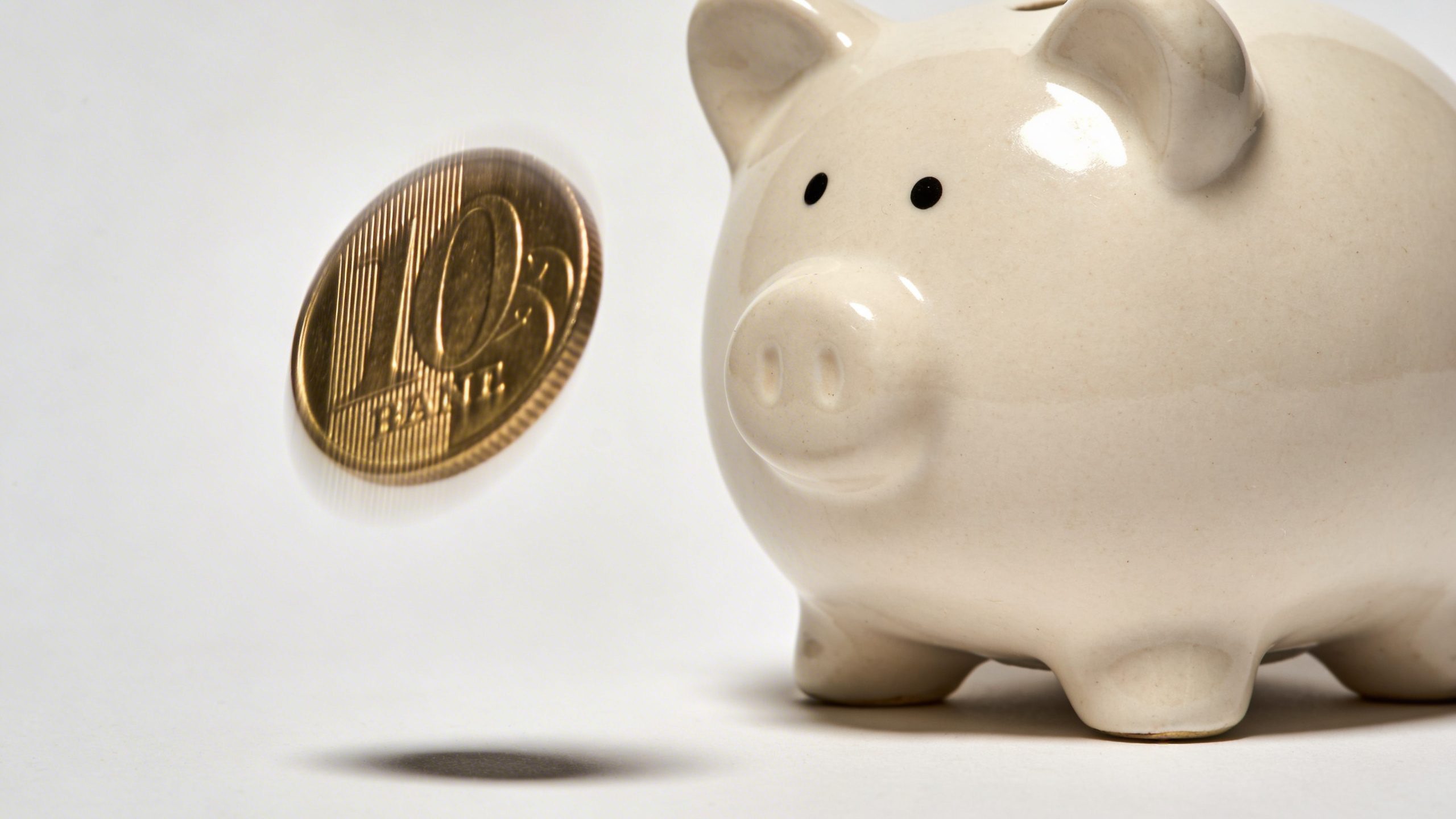 Closeup of a single piggy bank with a focused coin drop over a plain background
