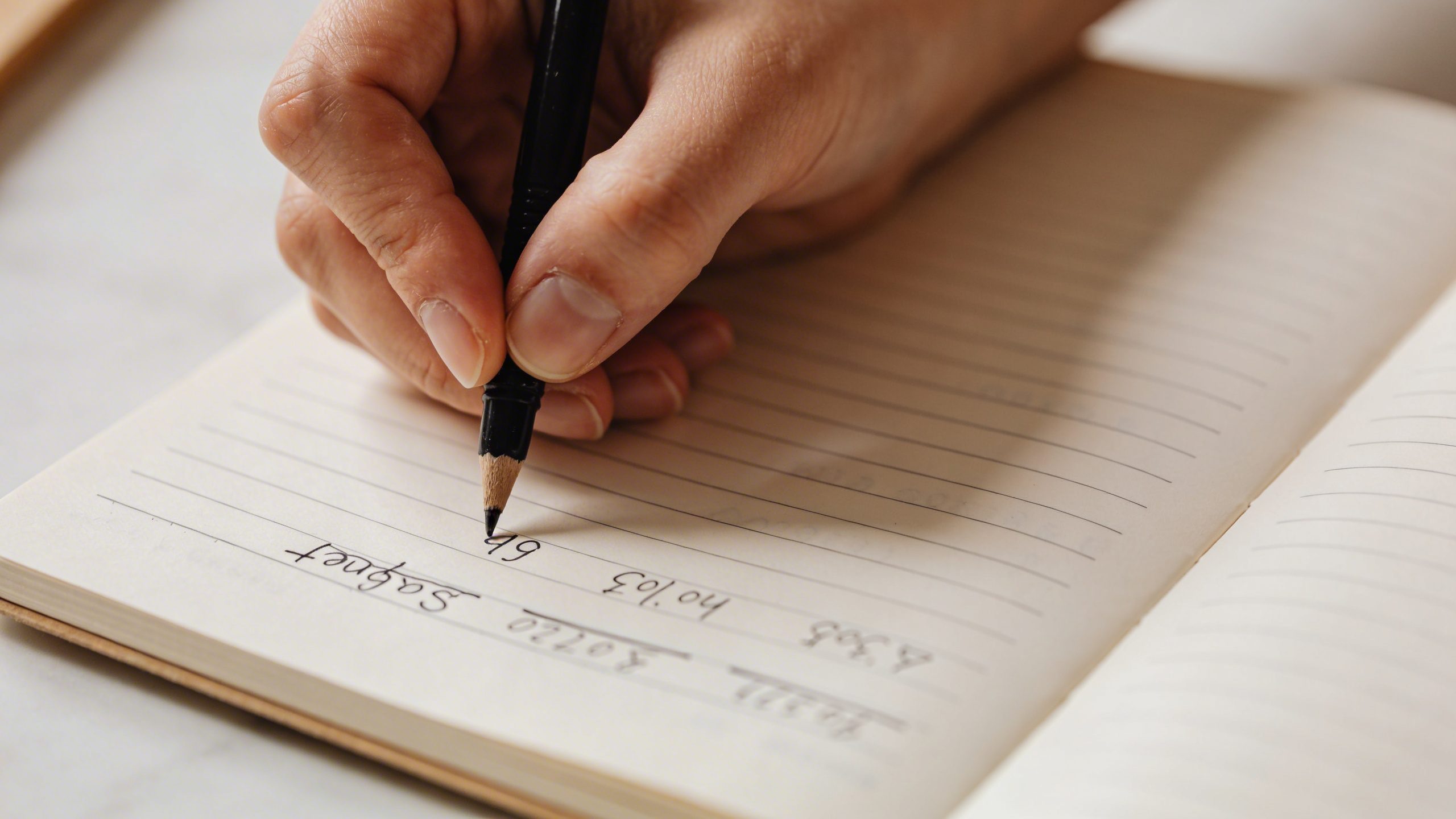 Closeup of a person’s hand writing a simple budget on a notebook