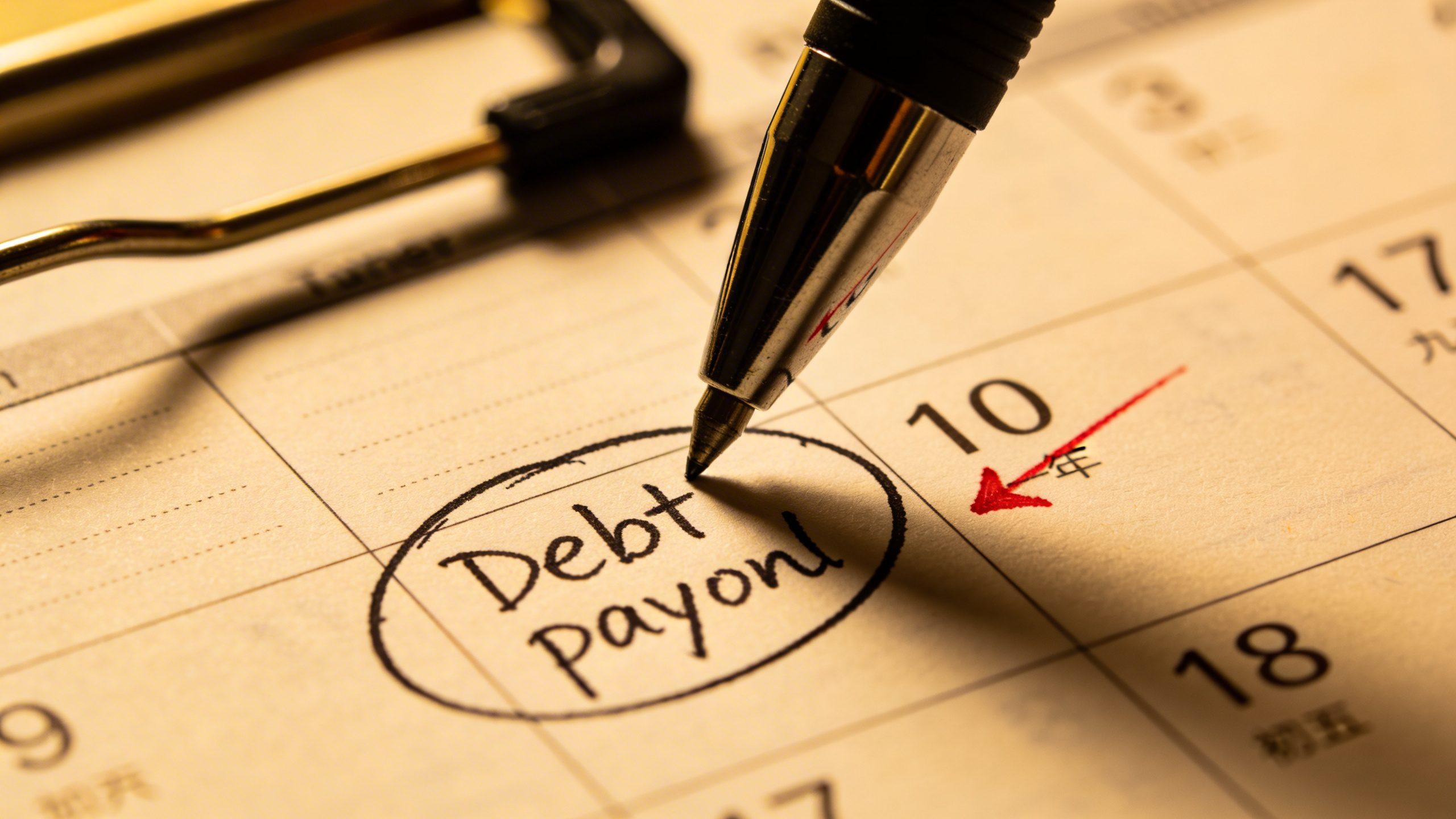 Closeup of a calendar page marking a debt payoff date with a pen