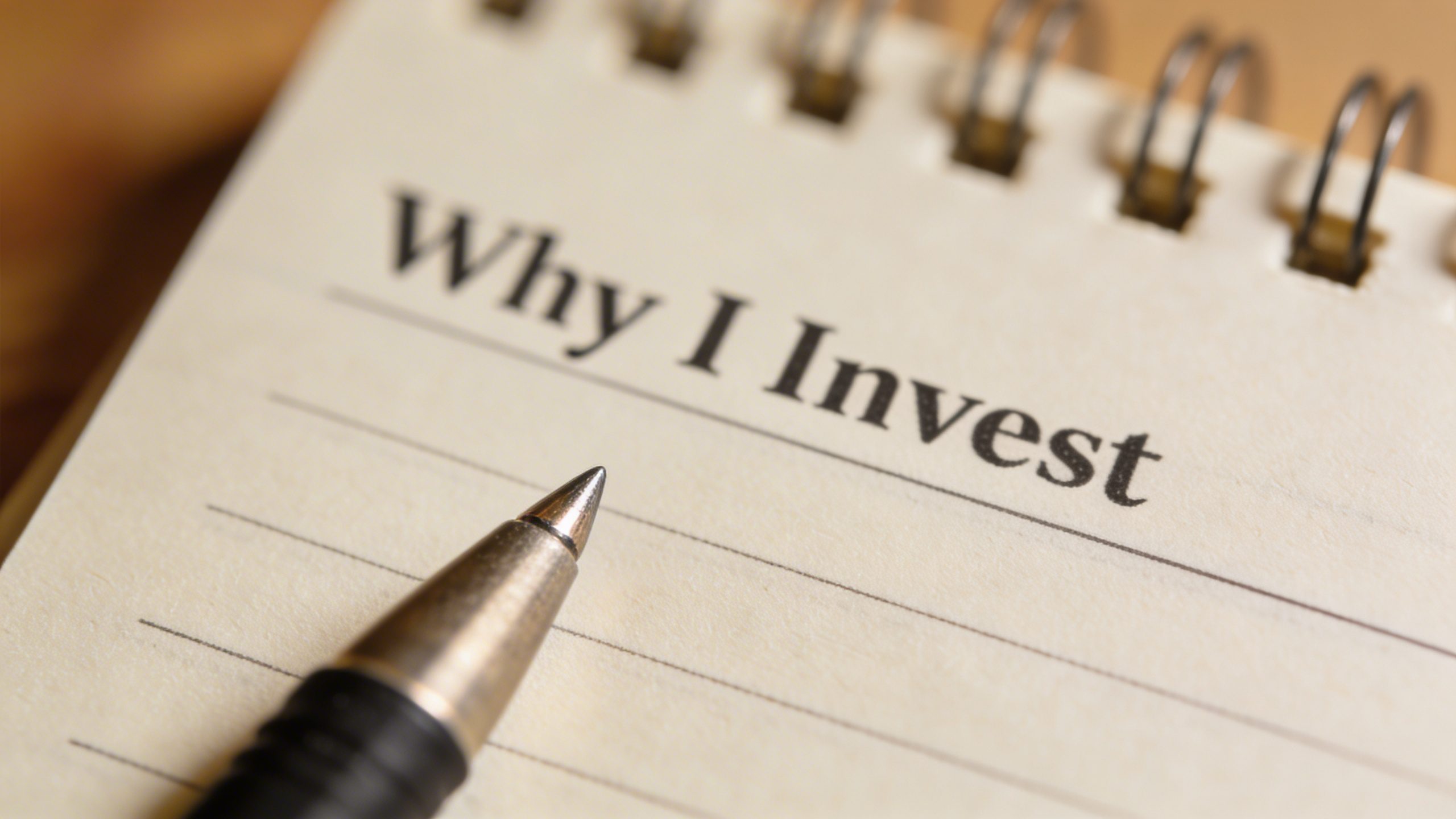 Closeup of a notebook page titled “Why I Invest” with a single pen tip