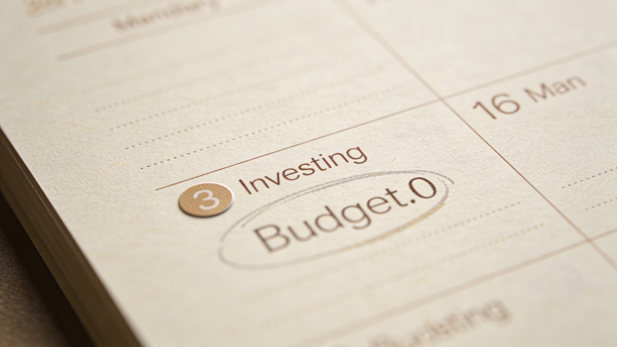 closeup of a single calendar page marking monthly investing date and budget