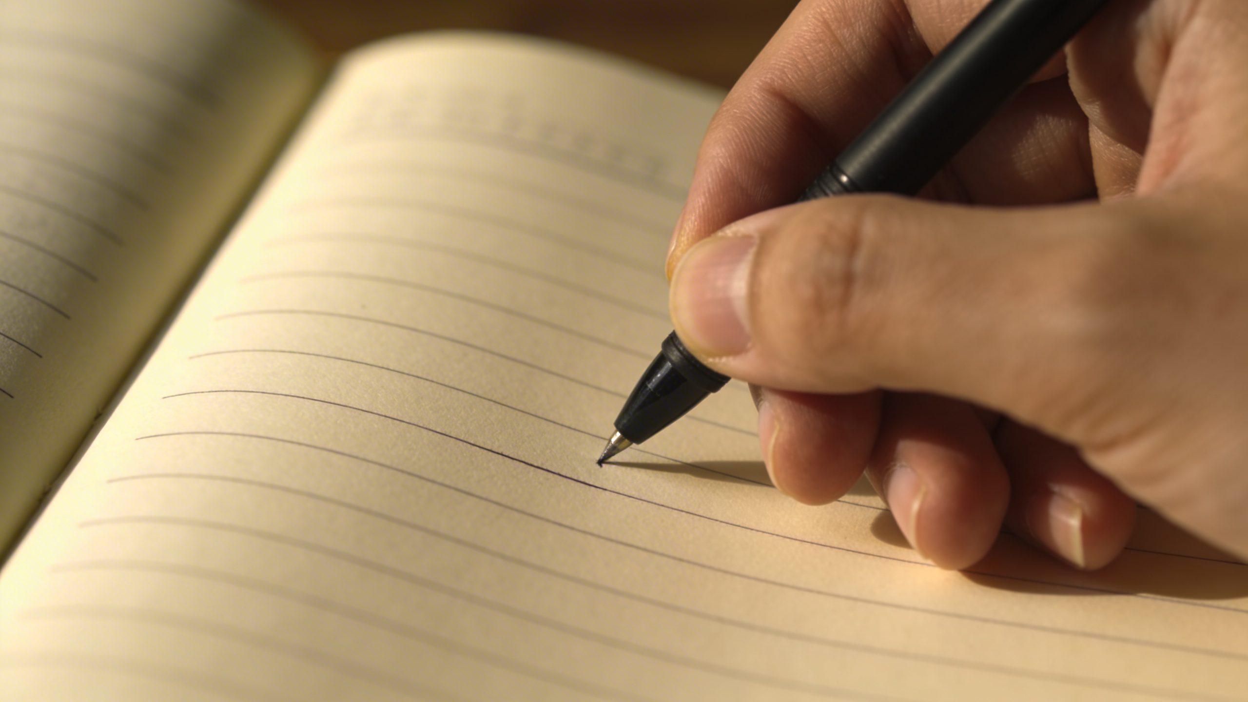 Closeup of a hand writing a small daily savings note on a notebook