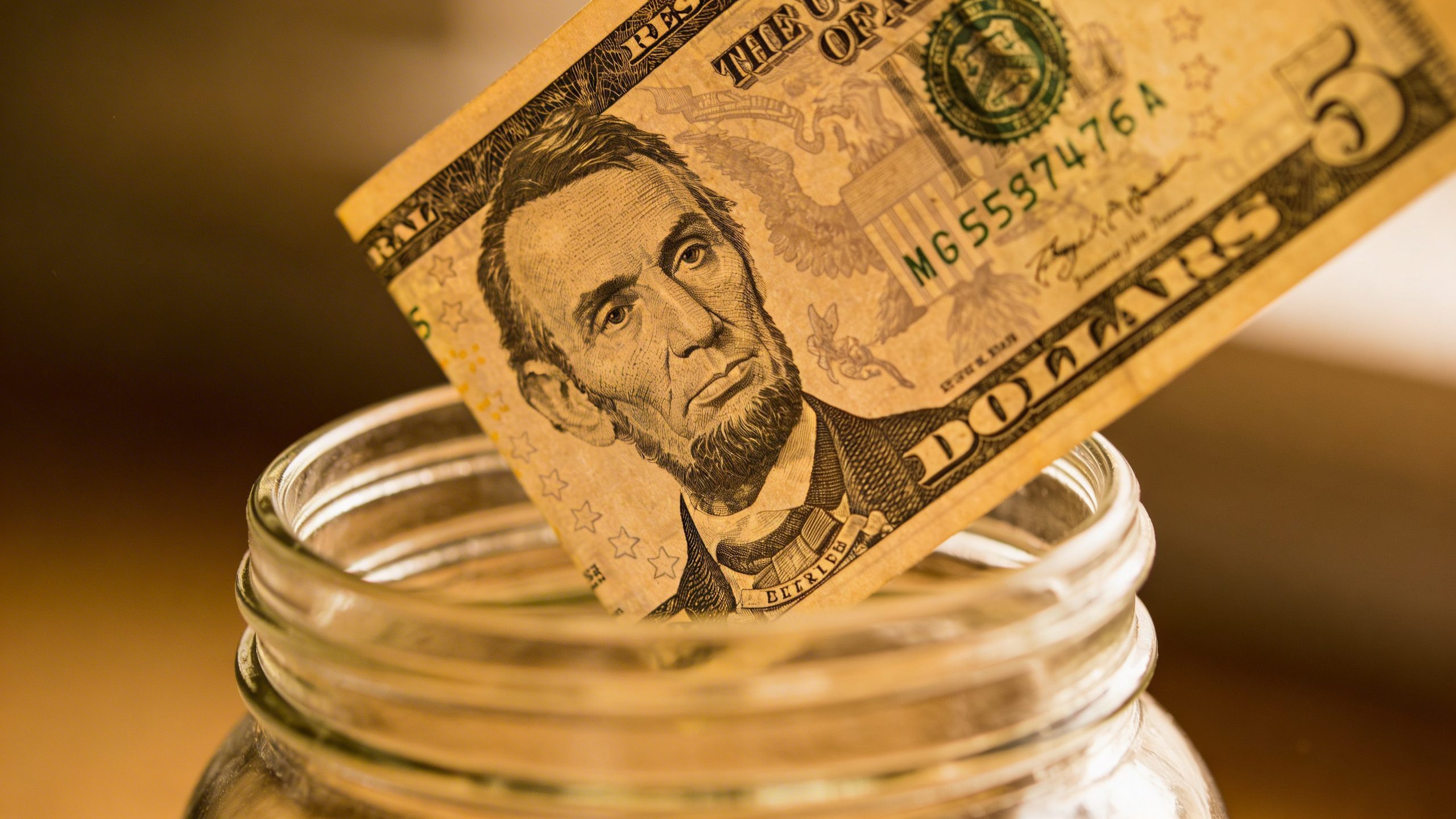 Closeup of a single $5 bill being set aside in a glass jar