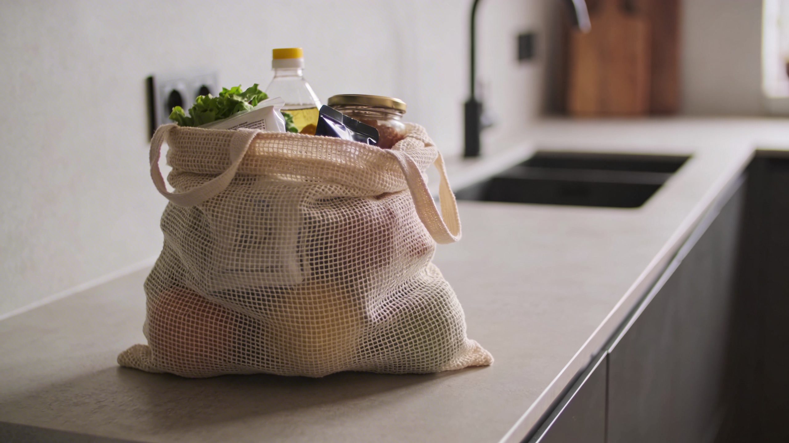 Closeup: one reusable grocery bag filled with essential items on a minimalist counter