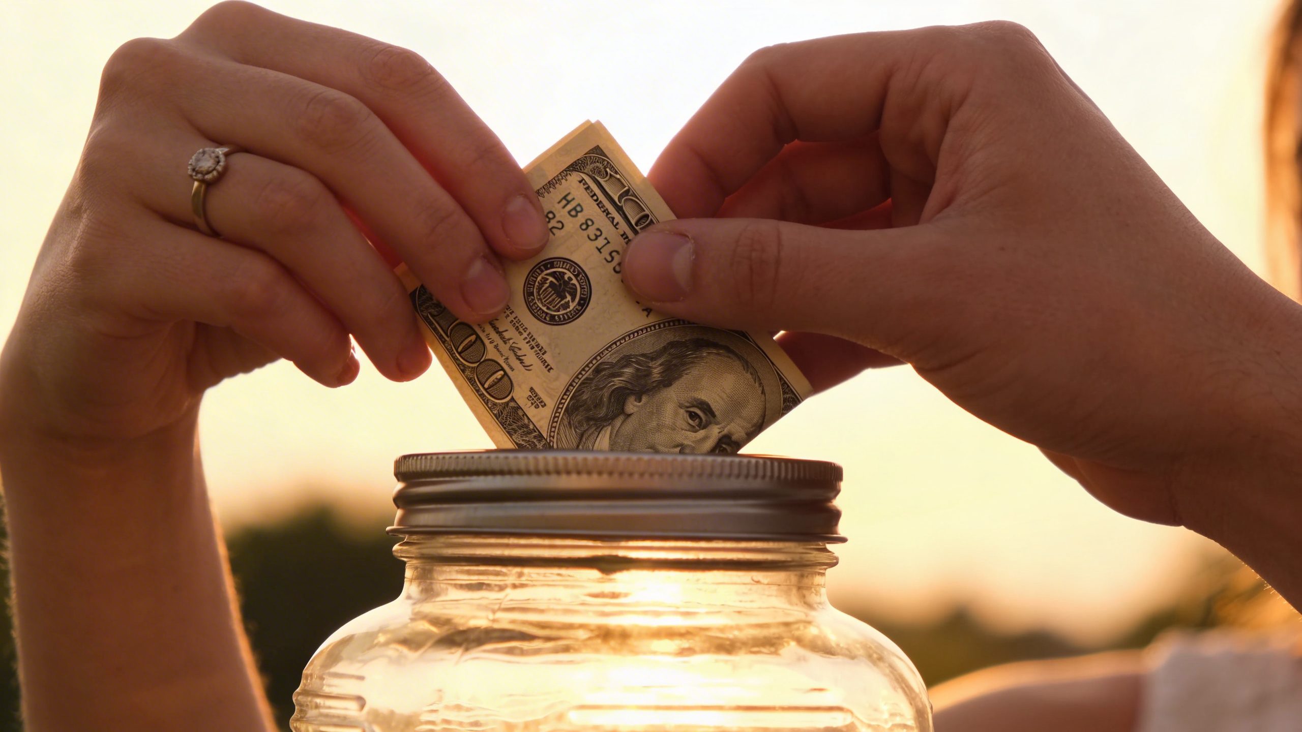 closeup of a couple’s hands placing a dollar into a labeled “Goal Pot” jar