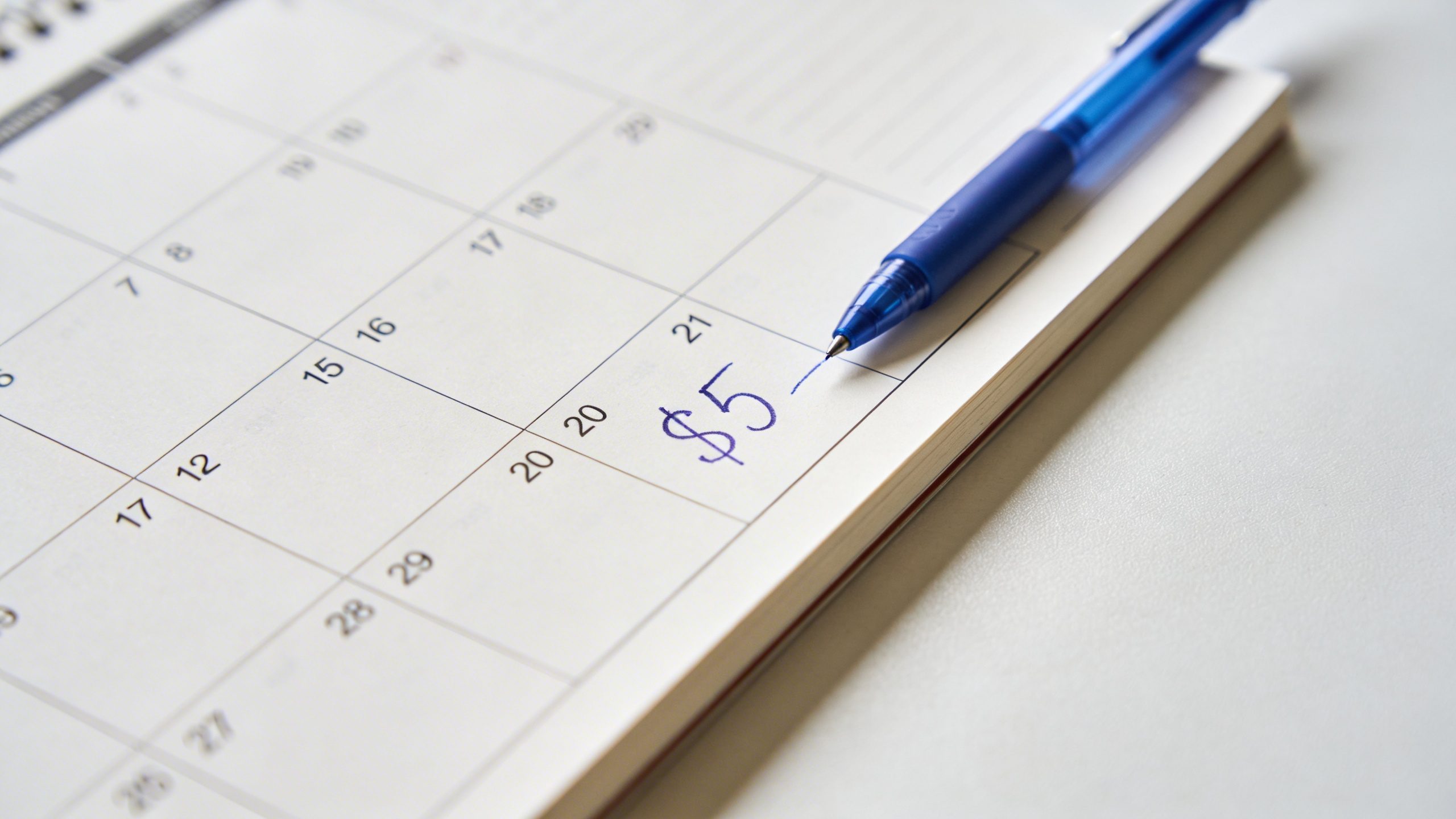 closeup of a calendar page marking a daily $5 savings note on a clean desk