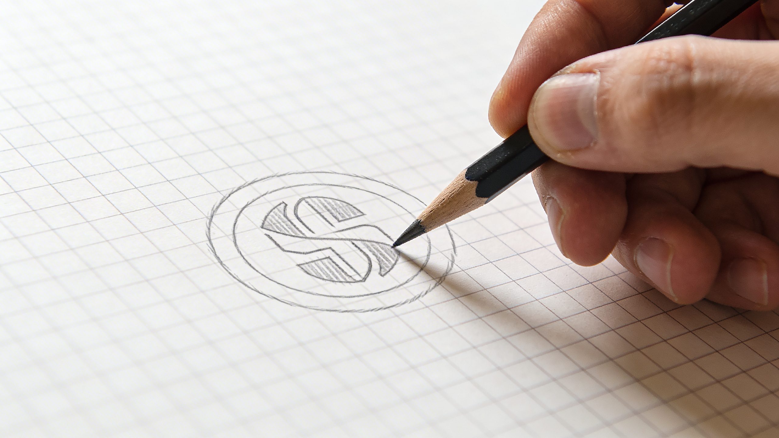 Closeup of a designer’s hand sketching a logo on grid paper