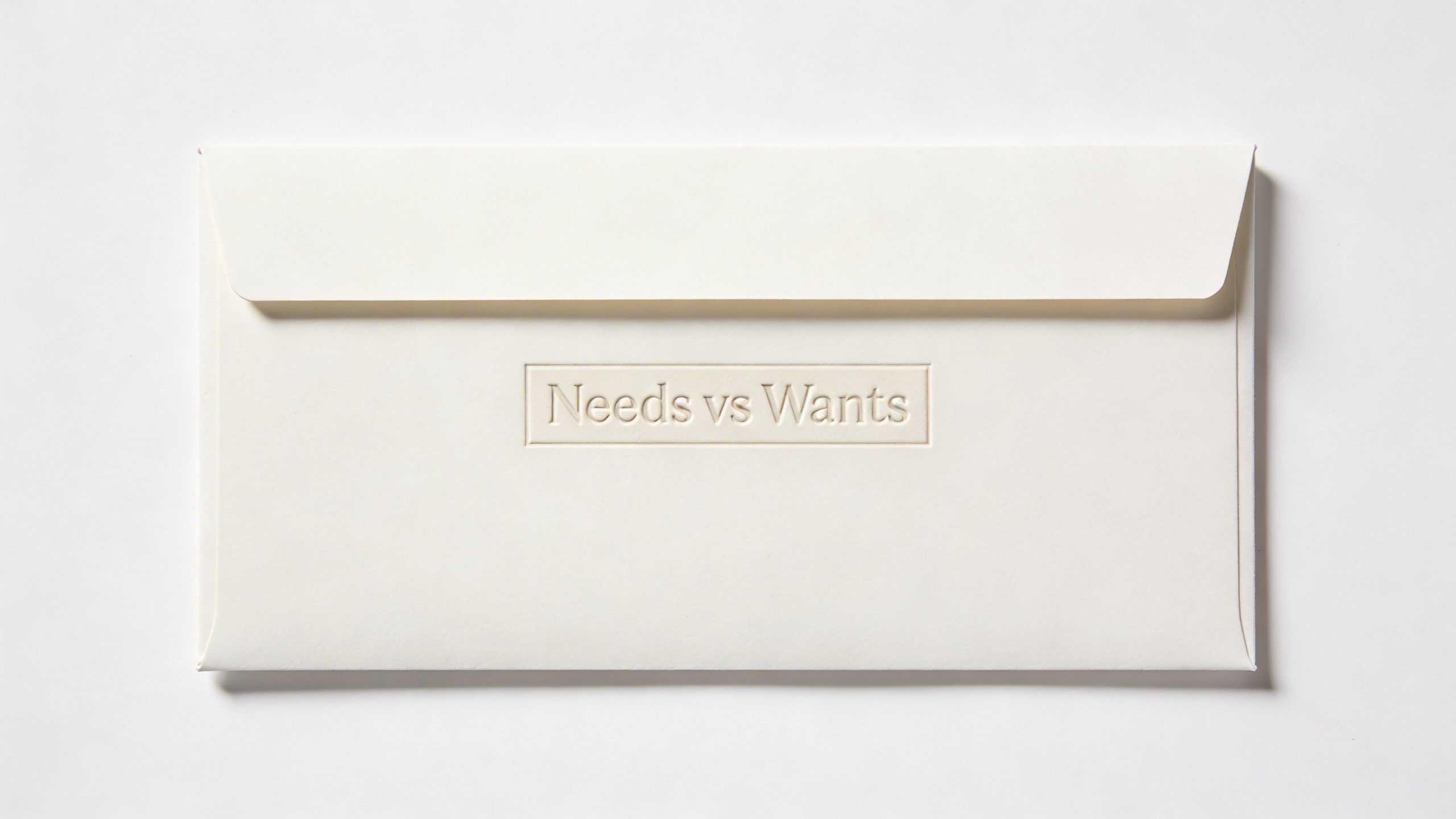 Closeup of a single family budget envelope labeled “Needs vs Wants” on white background