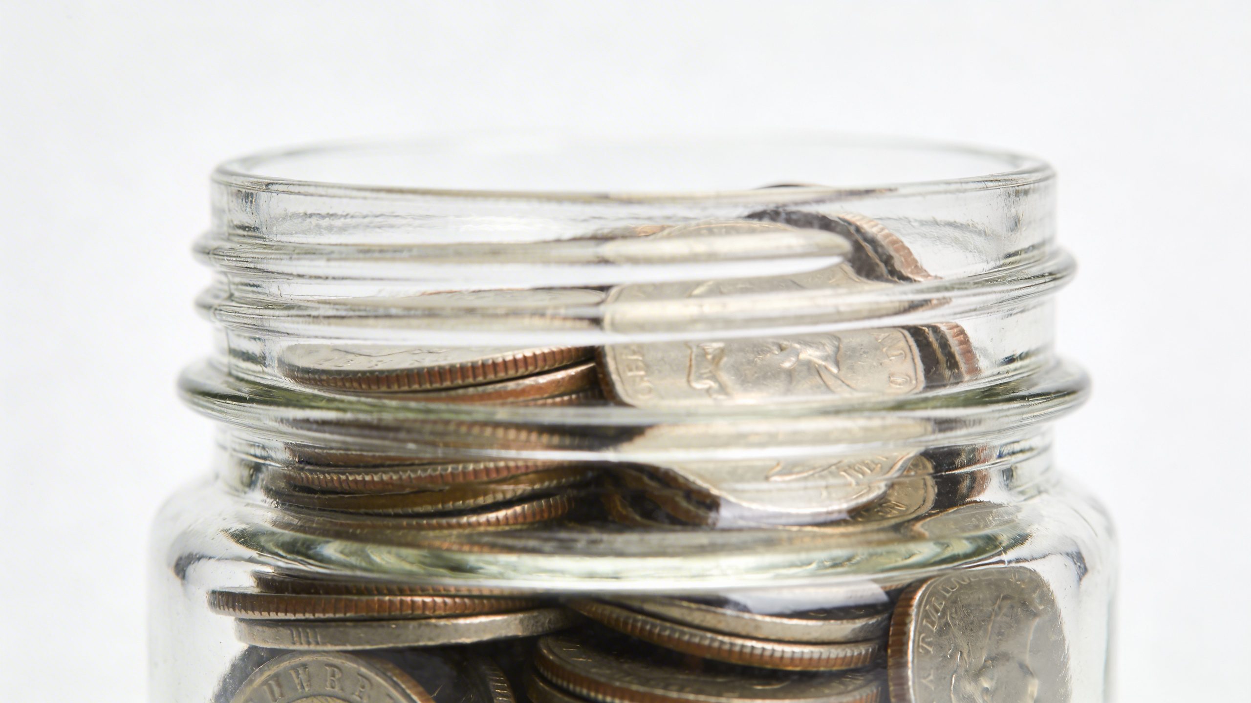 closeup of a glass jar with coins labeled 50/30/20 plan on white background