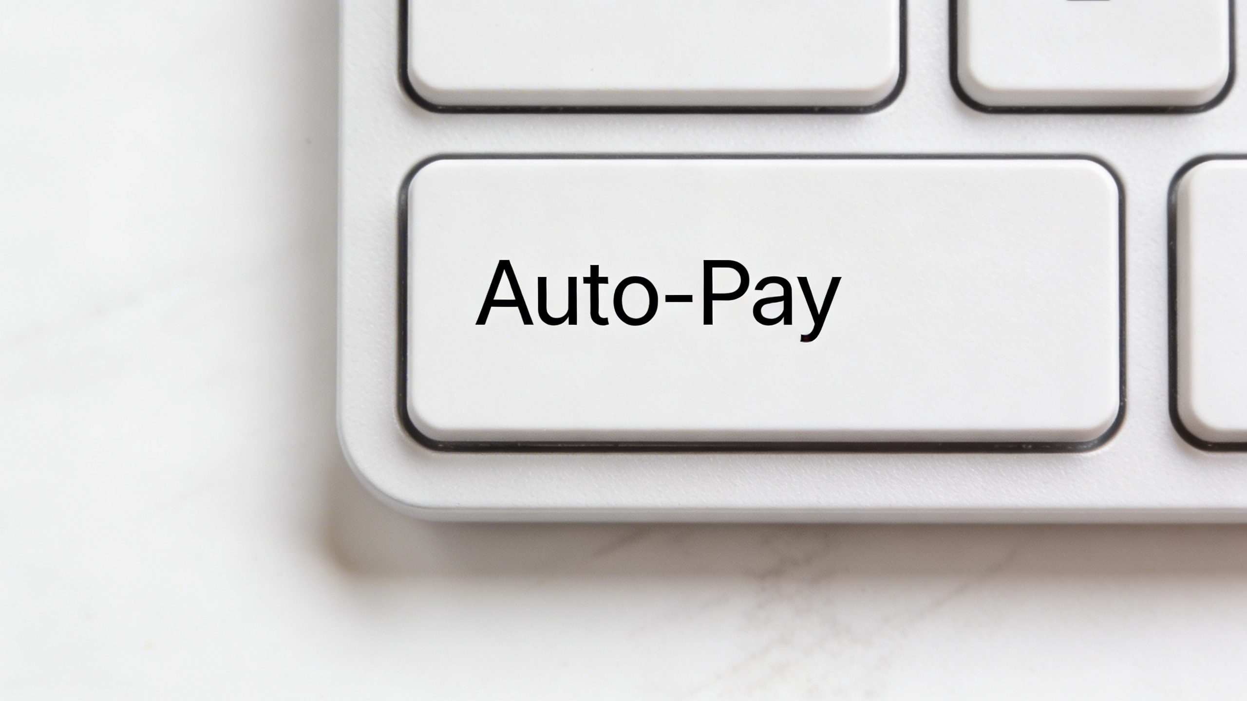 Closeup of a single keyboard key labeled “Auto-Pay” on a clean desk