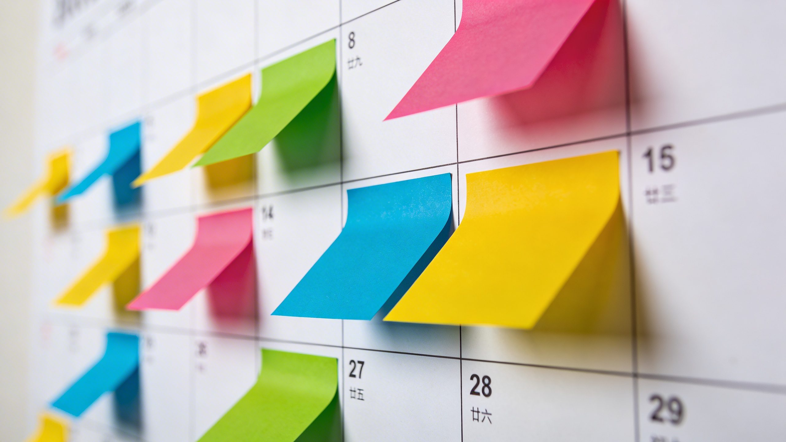 Closeup of color-coded debt payoff sticky tabs on a white wall-mounted printable calendar