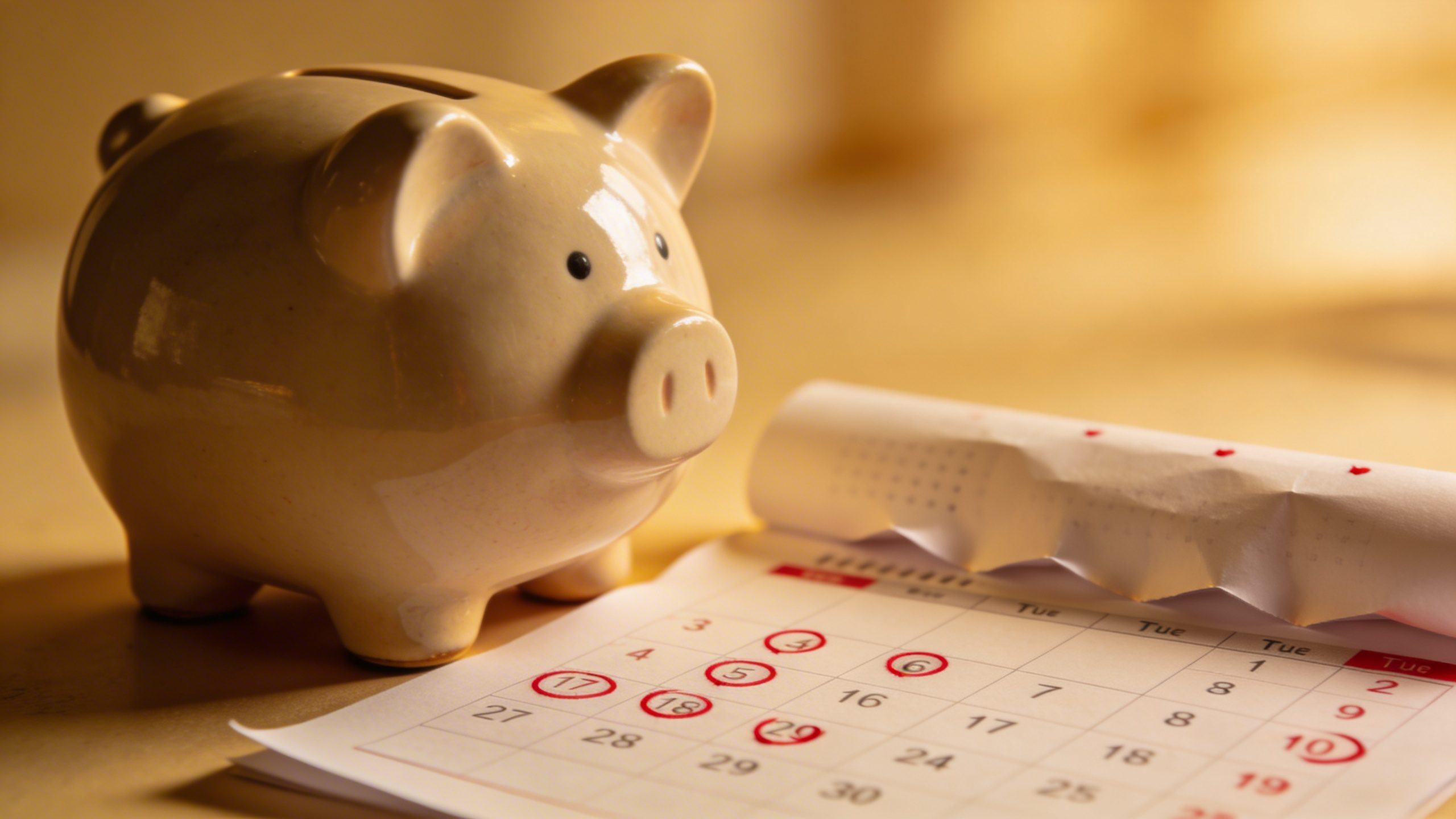 Closeup of a piggy bank beside a calendar with due dates marked