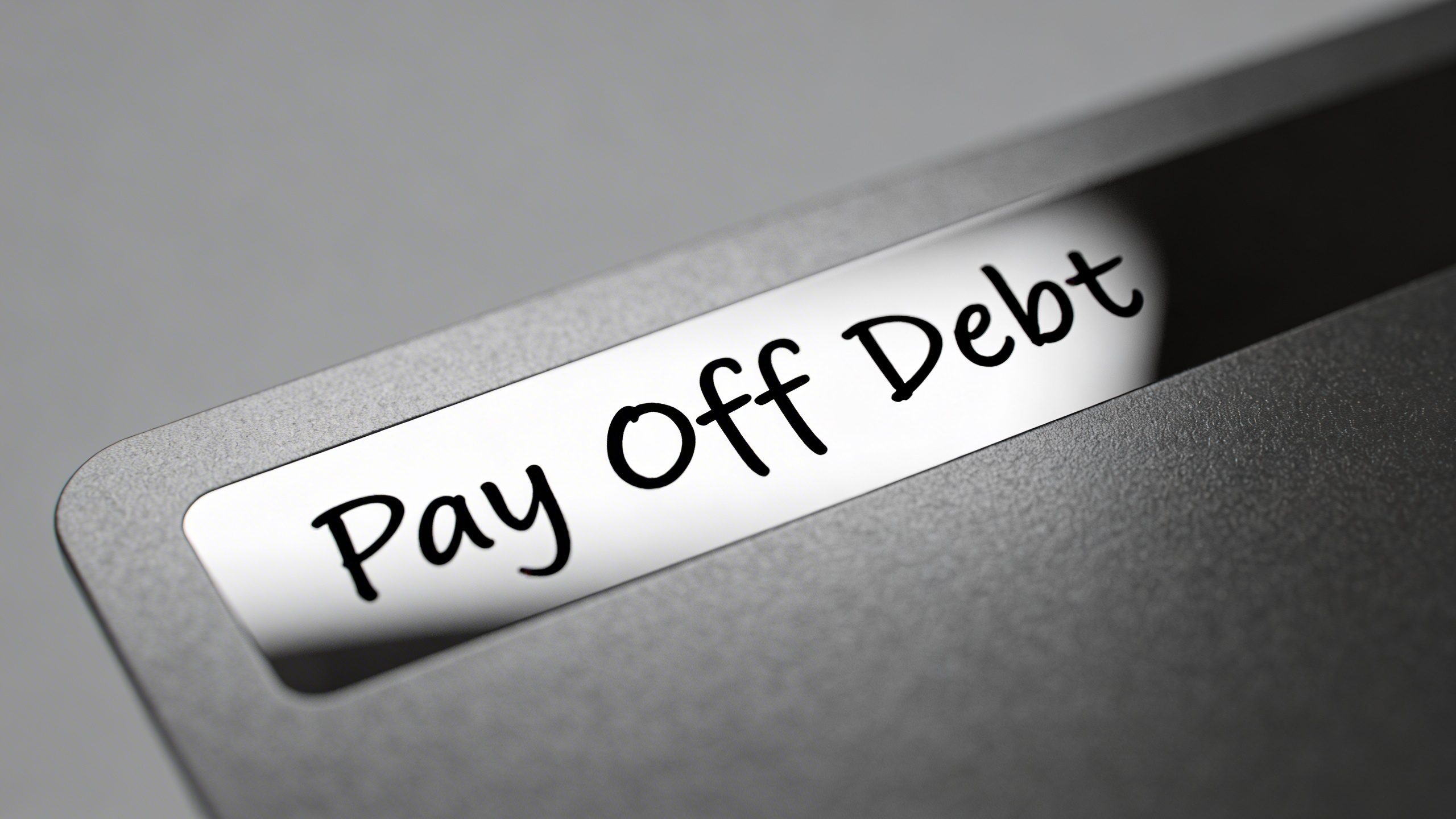 Closeup of a single credit card with a bold “Pay Off Debt” note reflected in the card’s shiny surface