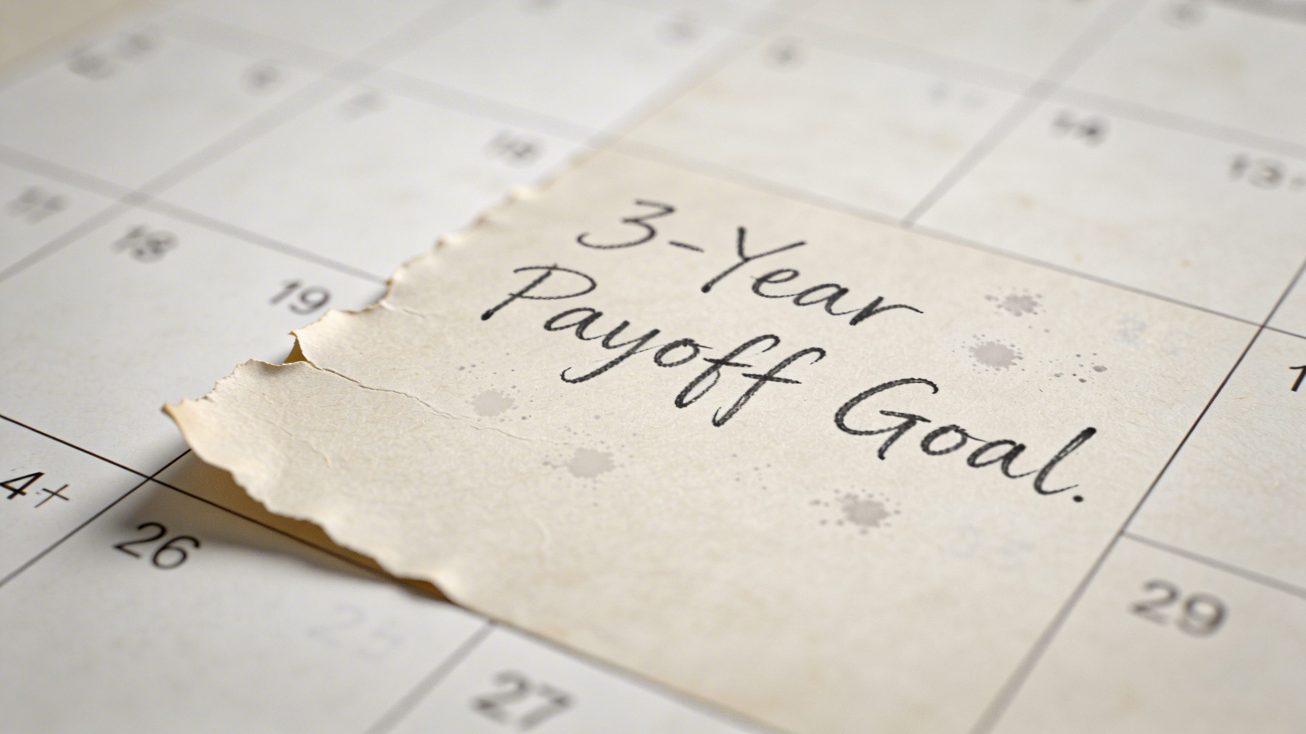 Closeup of a single calendar page showing a three-year payoff goal written in ink