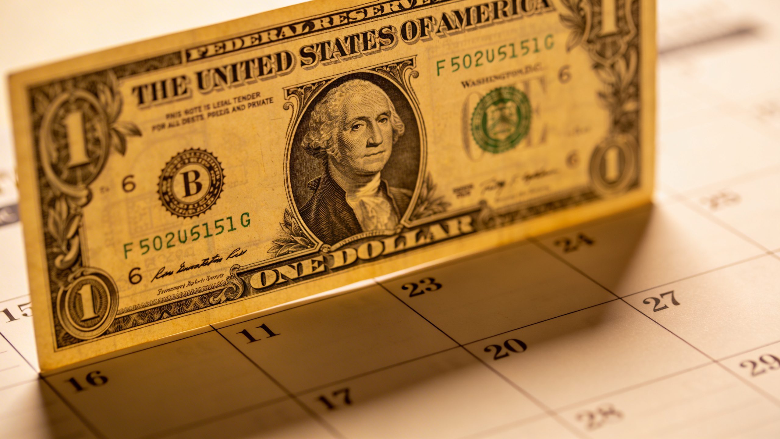 closeup of a single dollar bill atop a monthly debt calendar