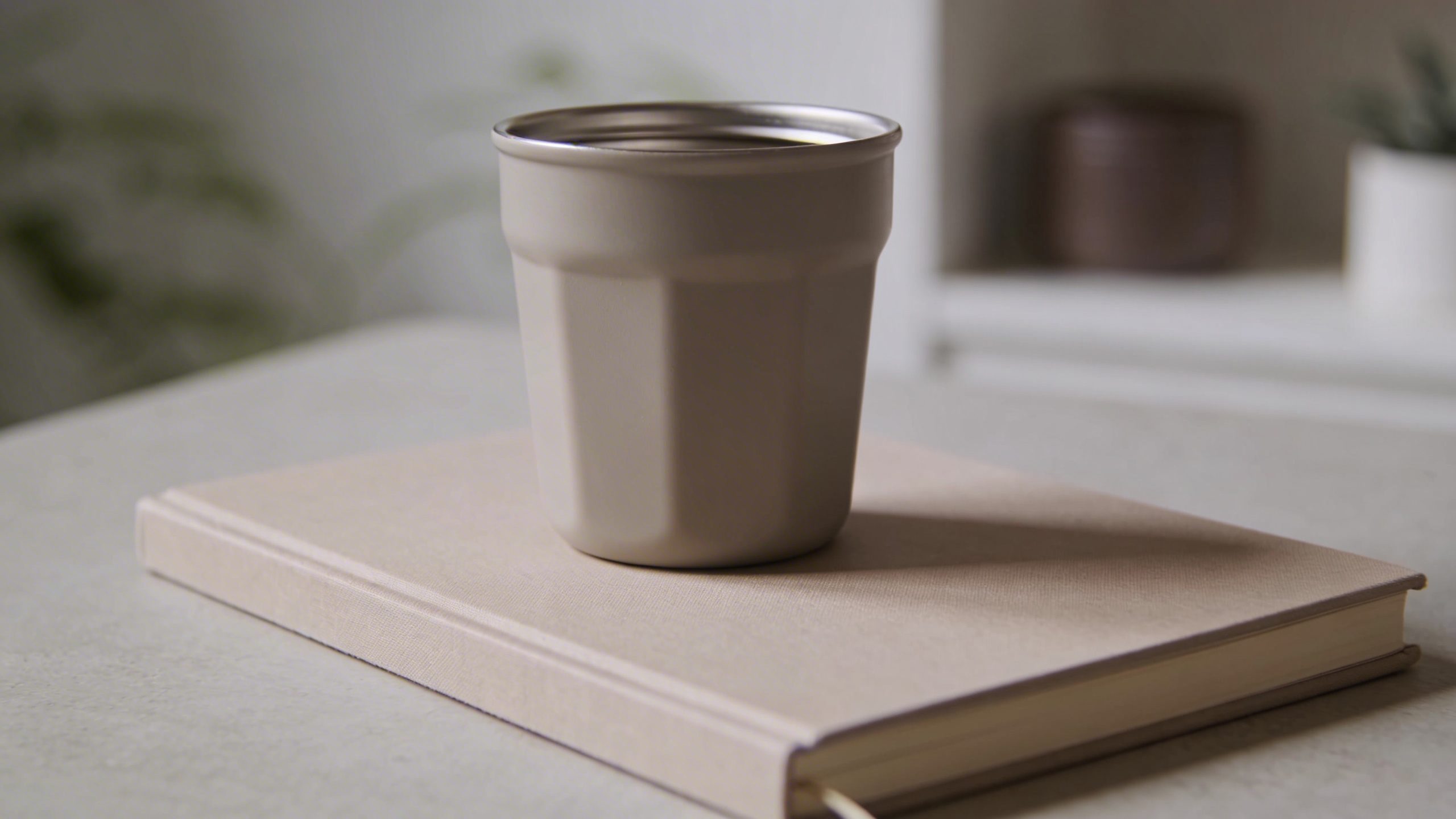Closeup of a lone reusable coffee cup atop a minimalist savings notebook